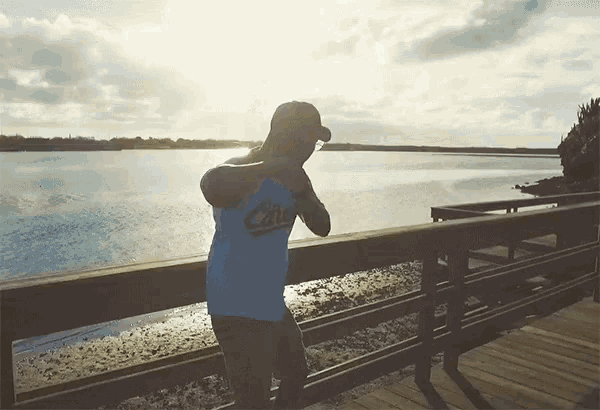 a man wearing a shirt that says ' california ' on it stands on a pier overlooking a body of water