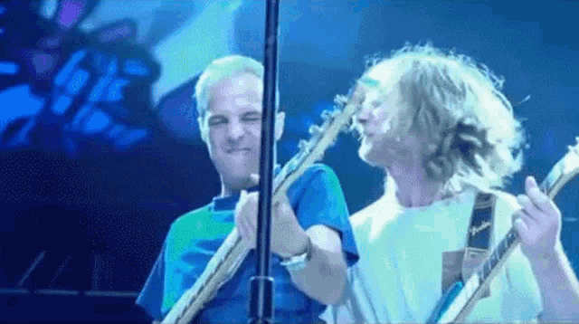 two men are playing guitars on a stage and one of them is making a funny face .