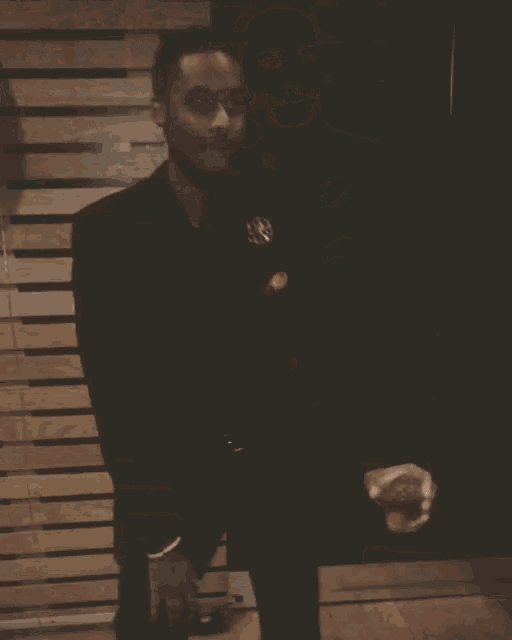 a man in a suit stands in front of a wooden wall holding a glass