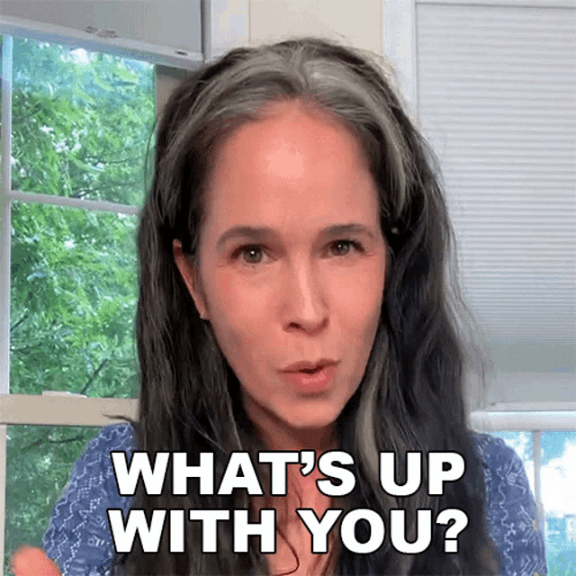 a woman says " what 's up with you " while standing in front of a window
