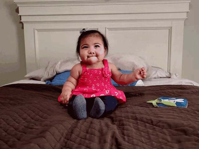 a baby girl in a pink dress sits on a bed next to a book