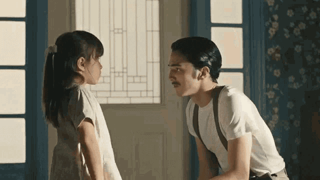 a man and a little girl are standing next to each other in front of a window .