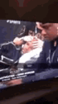 a man is holding another man 's head while watching a tv show .