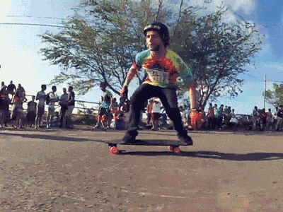 a man wearing a tie dye shirt and a helmet is riding a skateboard down a street
