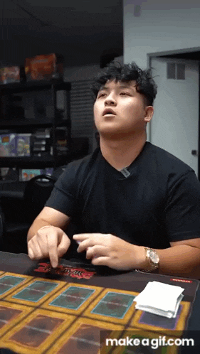 a man in a black shirt is playing yu gi oh on a table with cards on it
