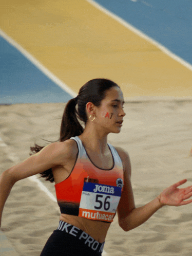 a woman wearing a joma top and a nike pro bottom is running on a track