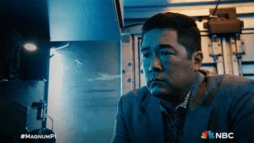 a man in a suit is sitting in a dark room with a nbc logo behind him