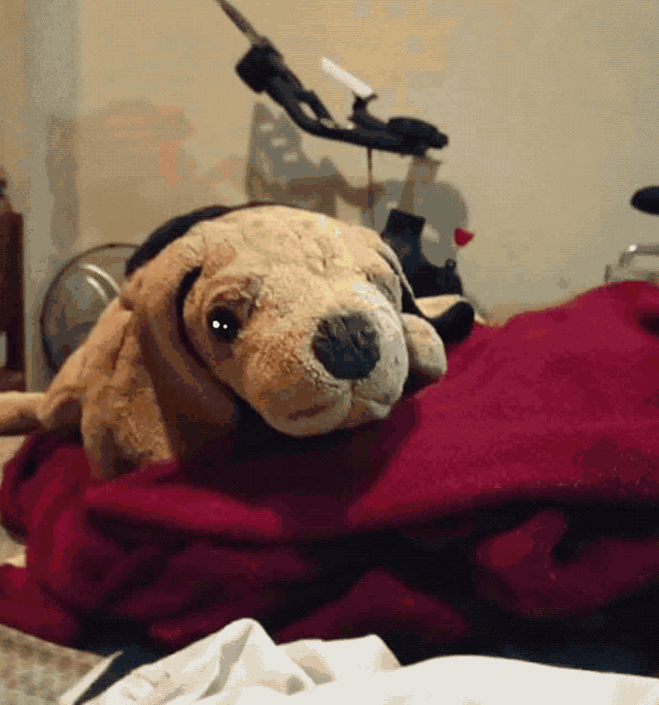 a stuffed dog is laying on a red blanket on a bed