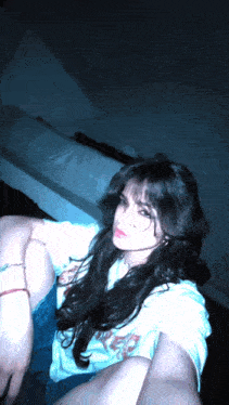 a woman taking a selfie in a dark room wearing a white shirt that says ' a ' on it