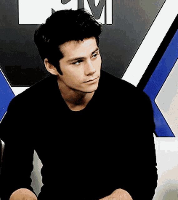a young man in a black shirt is sitting in front of a mtv sign