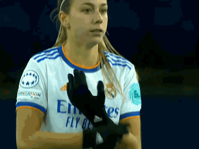 a female soccer player wearing a fly emirates shirt is putting on gloves .