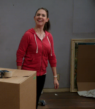 a woman wearing a red hoodie is standing next to a cardboard box