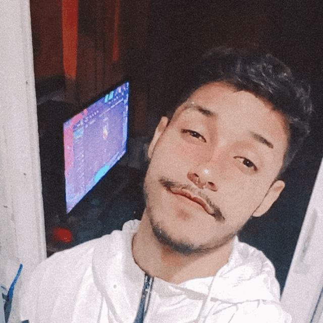 a man with a nose ring looks at the camera in front of a computer screen