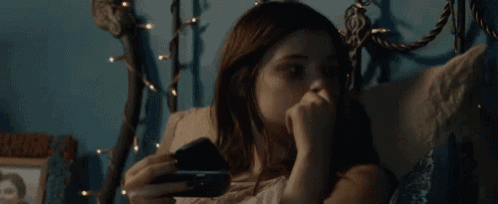 a young girl is laying in bed looking at her phone .