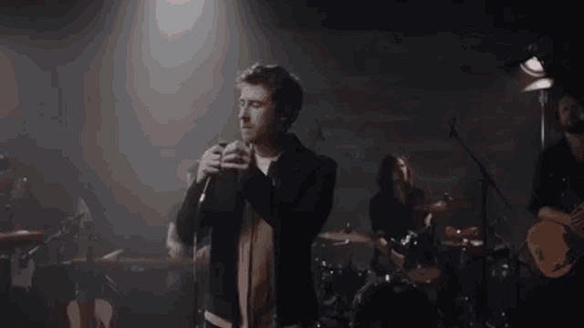 a man singing into a microphone in front of a band