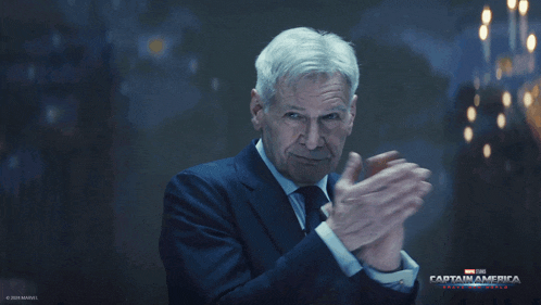 a man in a suit and tie is clapping in front of a captain america poster