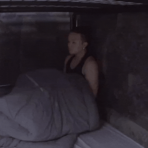 a person laying in a dark room with a blanket
