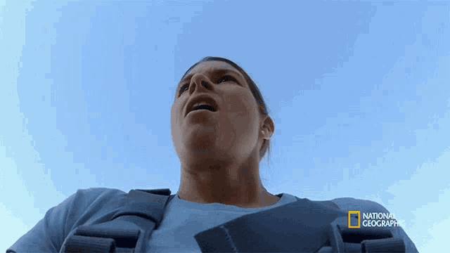 a woman in a national geographic vest looks up into the sky