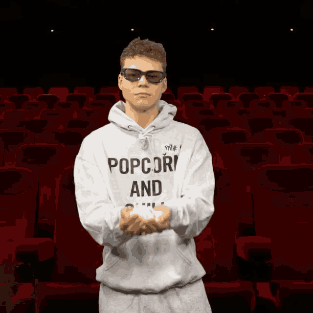 a man wearing a hoodie that says popcorn and chill holds popcorn in his hands
