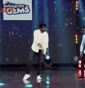 a man in a white jacket is dancing on a stage in front of a blue background .