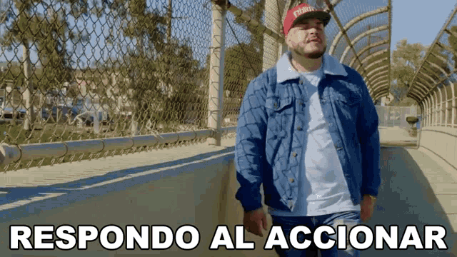 a man wearing a denim jacket and a red hat stands on a bridge with the words respondo al accionar below him