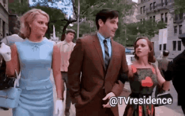 a man in a suit and tie is walking with two women on a city street .