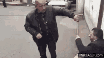 two men are standing next to each other on a sidewalk holding a stick .