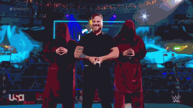 a man in a black shirt is standing in front of two people in red robes with the word usa on the bottom right