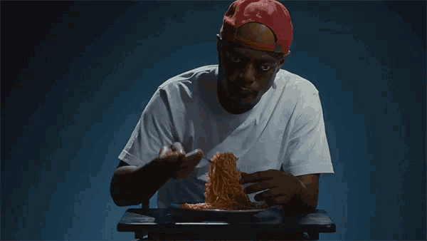 a man wearing a red hat is eating spaghetti with a fork and knife