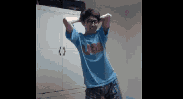 a man wearing glasses and a blue shirt is standing in front of a wardrobe .