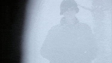 a man in a black jacket and helmet is standing in the fog holding a gun .