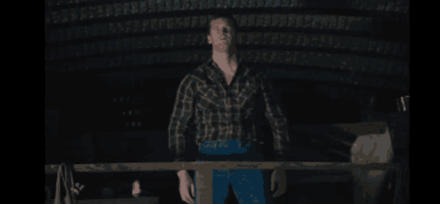a man in a plaid shirt and blue jeans is standing in the dark