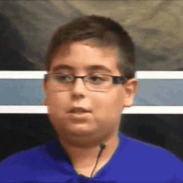 a young boy wearing glasses and a blue shirt is speaking into a microphone