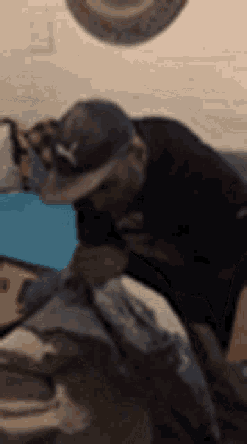 a man wearing a hat is sitting on a couch with his head down .