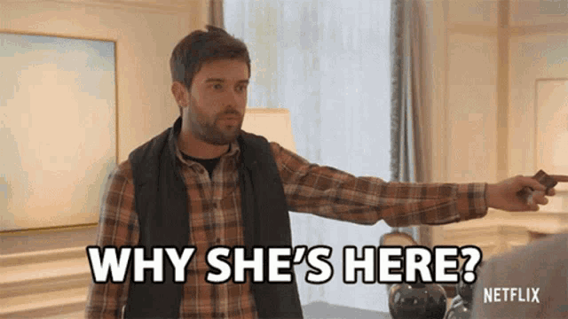 a man in a plaid shirt is pointing at something and says why she 's here