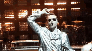 a man wearing sunglasses and a silver jacket is singing on stage