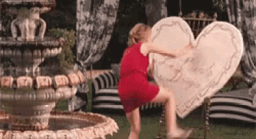 a woman in a red dress is standing next to a large heart shaped item .