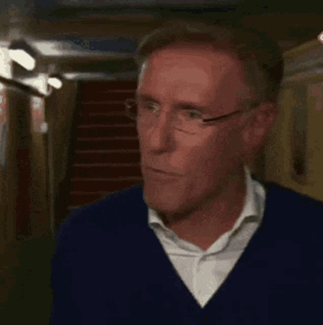 a man wearing glasses and a blue sweater holds his fist up