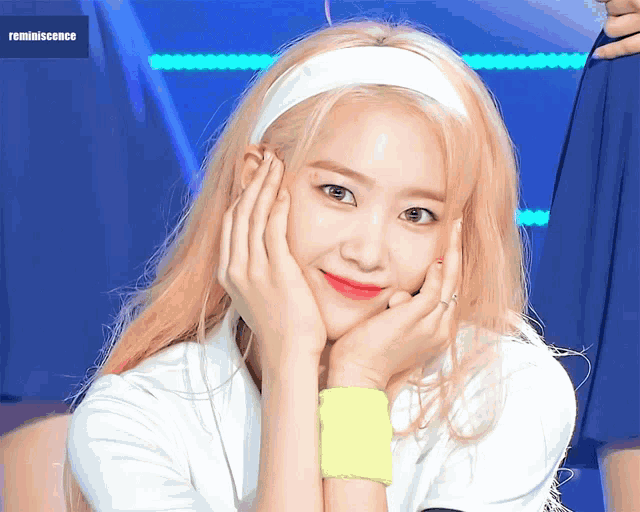 a woman with blonde hair wearing a white headband and a yellow wristband looks at the camera
