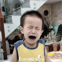 a young boy is crying and wearing a yellow shirt that says doraemon
