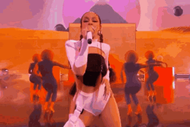 a woman is singing into a microphone on a stage while a group of dancers are dancing behind her .
