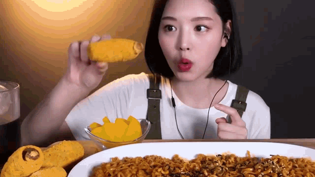 a woman is eating corn on the cob and a plate of noodles