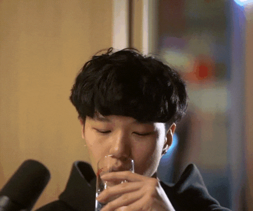 a young man is drinking from a glass in front of two microphones