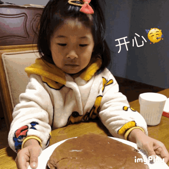 a little girl is sitting at a table with a plate of food and the word imgplay is above her head
