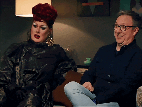 a drag queen and a man sit on a couch