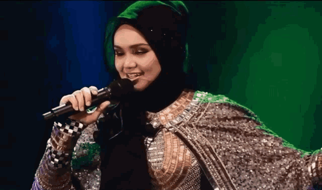 a woman is singing into a microphone with a green background