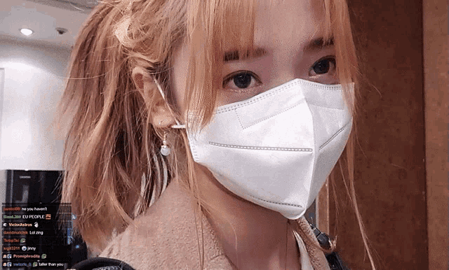 a woman wearing a white face mask with a ponytail looks at the camera