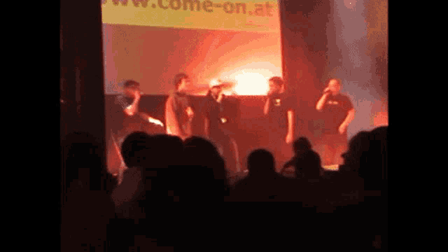 a group of people standing in front of a large screen that says come-on.at