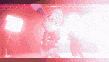 a girl in a red dress is dancing on a stage in front of a pink light .