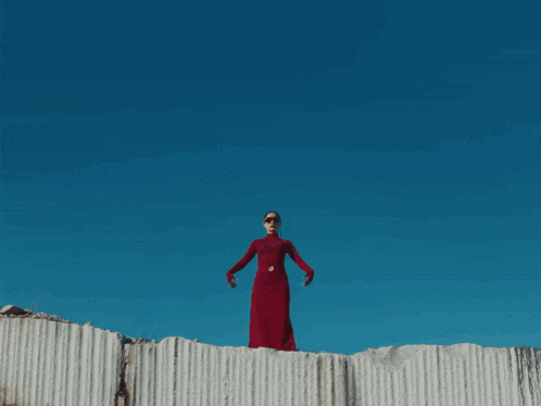 a woman in a red dress stands in front of a huge explosion